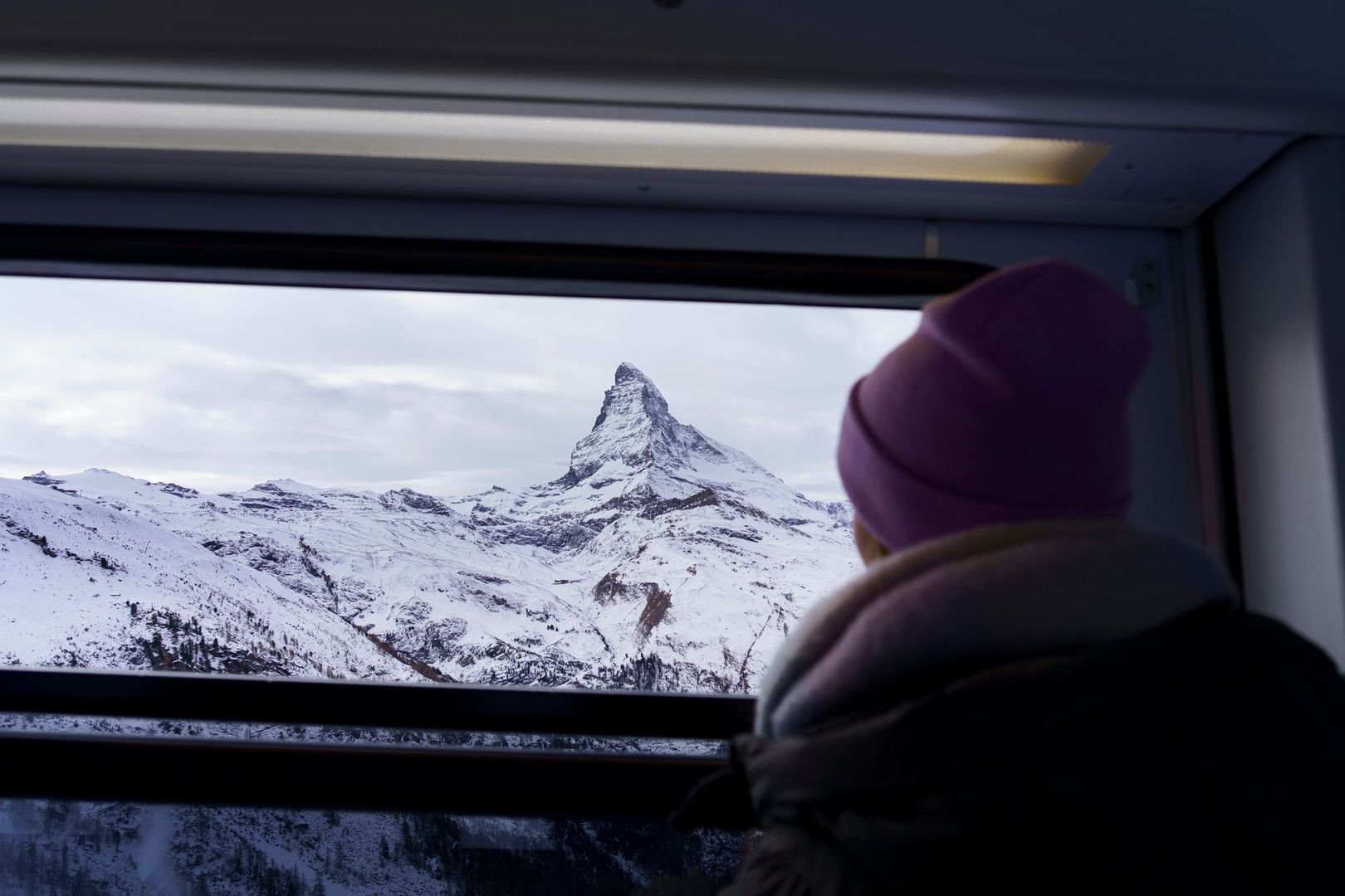Resenär ser snöklädda alper genom tågfönstret